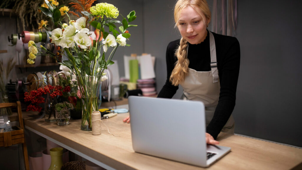 A young blonde female stands at her desk with flowers, reading an article on her laptop about the process of applying for a lithuania business visa