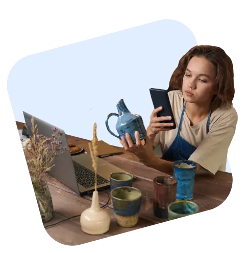 Ceramics maker checking her phone next to a laptop