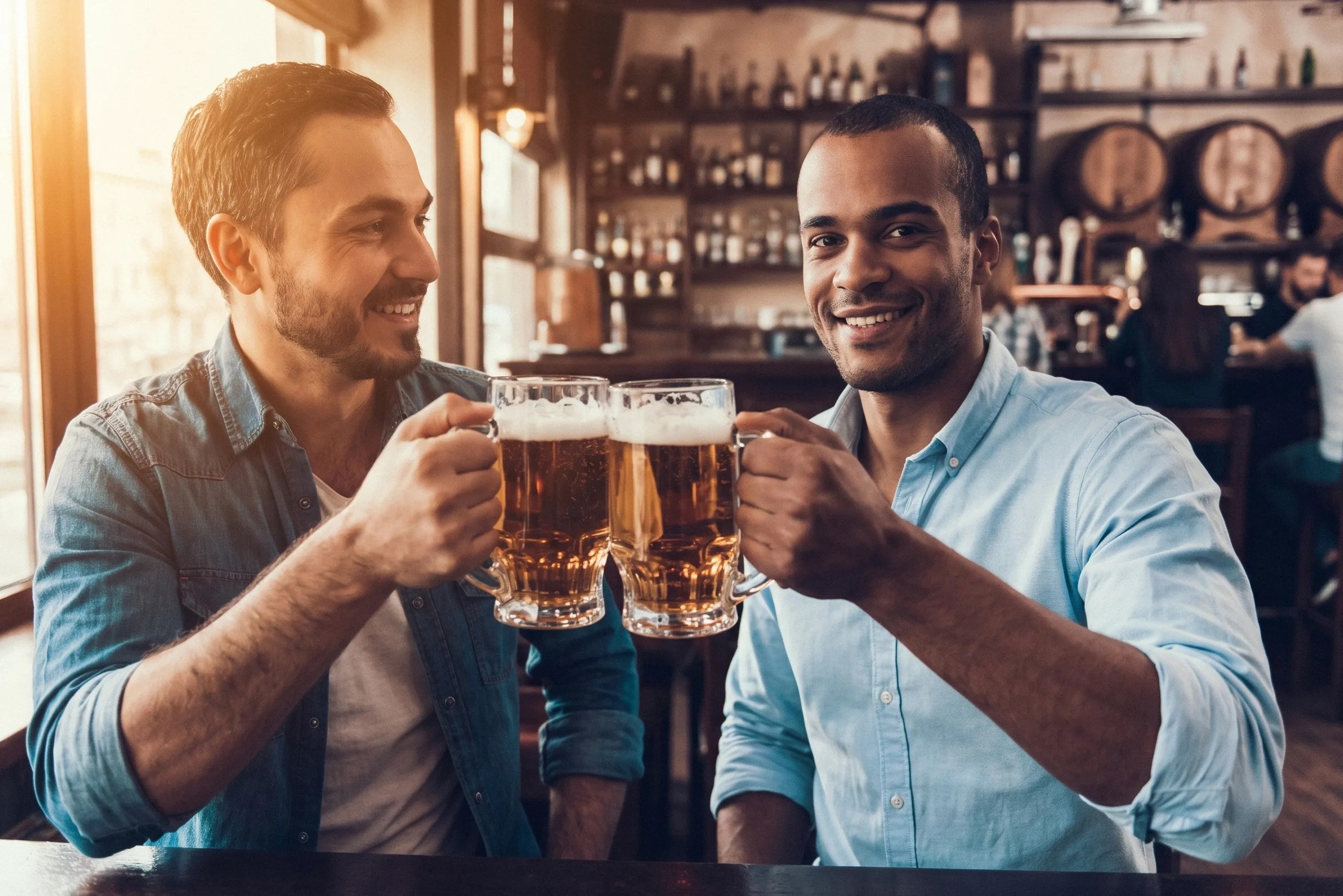 Two men with glasses of beer clink their drinks together