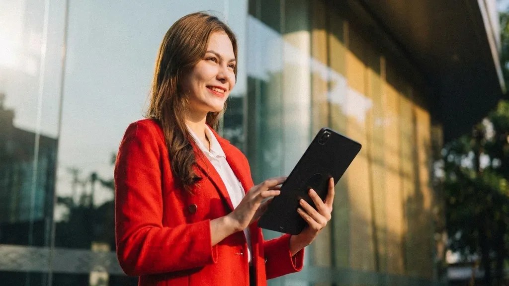 A young brunette female in a red suit stands outside and smiles as she reads an article on her ipad about 'Is Wise Business safe?'