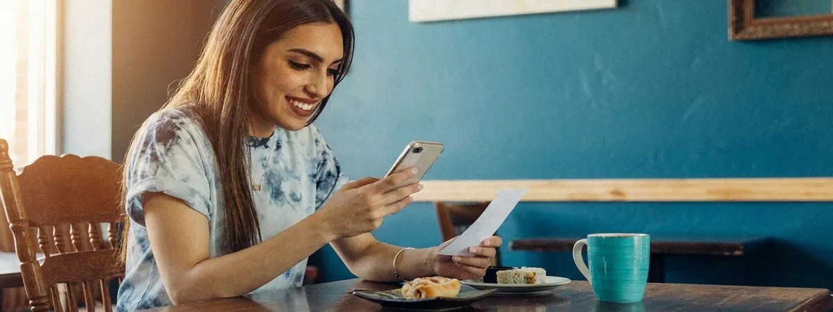 A lady sits down at the table and looks at her phone. There are framed pictures in the background