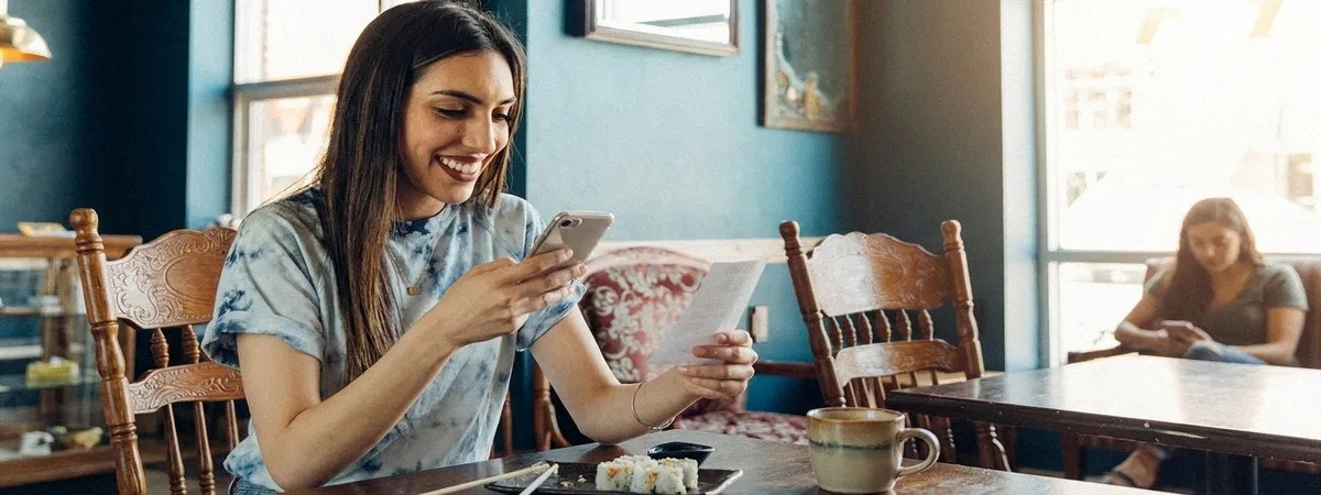 A lady sits down at the table and looks at her phone. There are framed pictures in the background