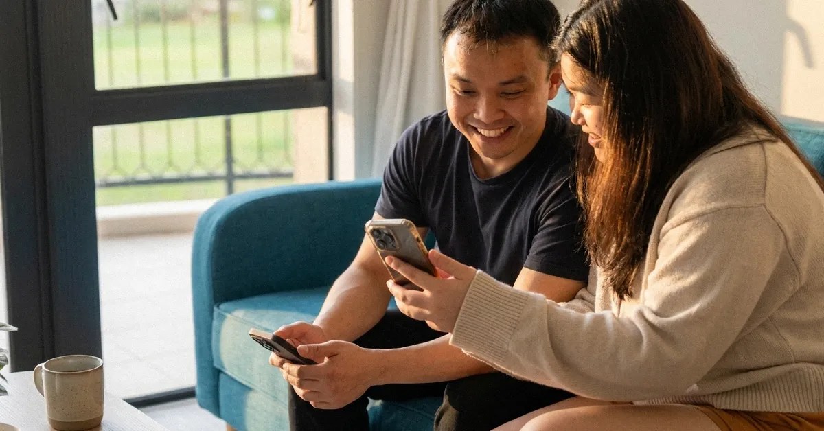 A man and woman sit on a sofa and look at a device as they navigate the cost of living in the Phillippinees