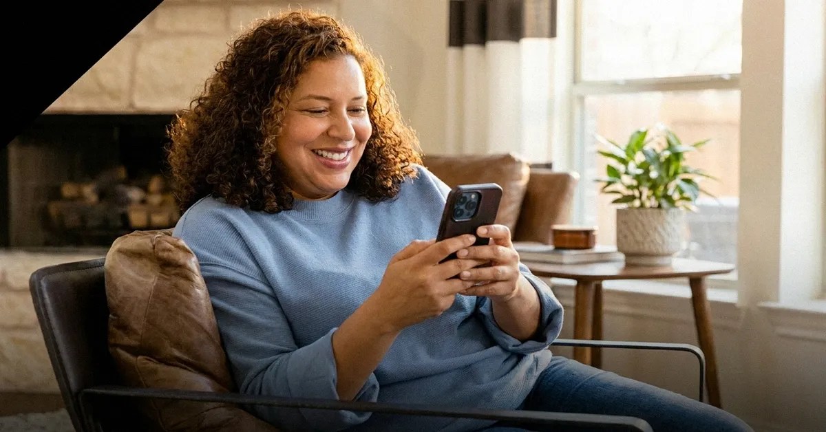 A woman sits on the sofa, holding her phone and reading an article about Wise vs Western Union